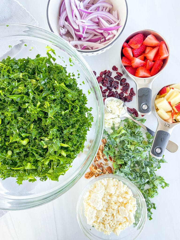 This is a photo of a bowl of fresh, chopped kale, alongside additional toppings for the kale salad. 