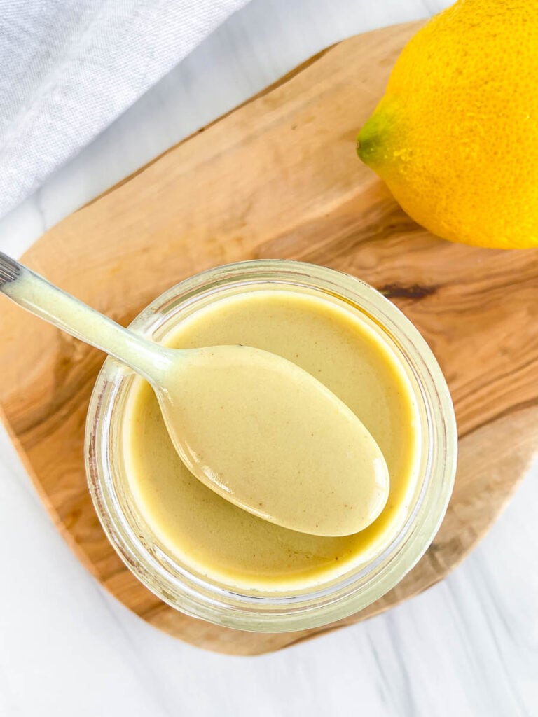 This is a photo of homemade honey mustard Greek yogurt dressing in a small mason jar next to a lemon. 
